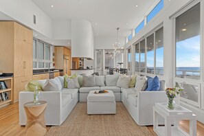 A modern living room with a sectional sofa, a coffee table, and a view of the ocean through large windows. - Gulf-Front Retreat • Pool + Golf Cart • Near Gulf Place | Matarangi (Santa Rosa Beach)