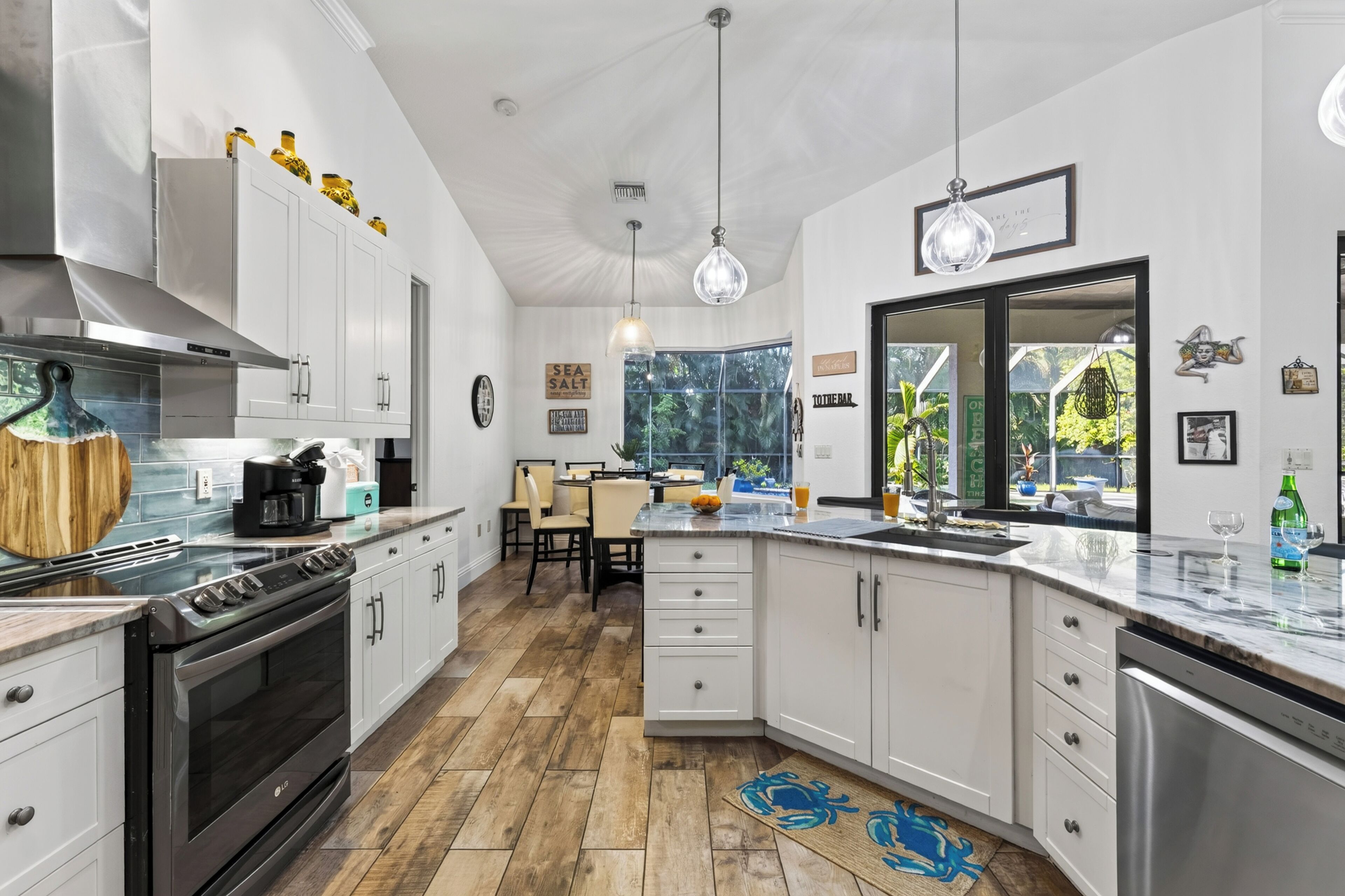 A modern kitchen with white cabinetry, a built-in oven, and a dining area with a view of the outdoors.
