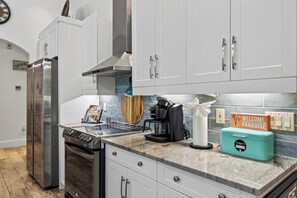 A modern kitchen with white cabinets, stainless steel appliances, a coffee maker, and a sign welcoming guests. - Screened Pool + Outdoor Kitchen + Fire Table | Beaches | A Peaceful Paradise (Naples)