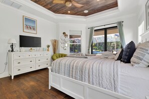 A bedroom with a bed, a dresser, a television, and a ceiling fan. - Screened Pool + Outdoor Kitchen + Fire Table | Beaches | A Peaceful Paradise (Naples)