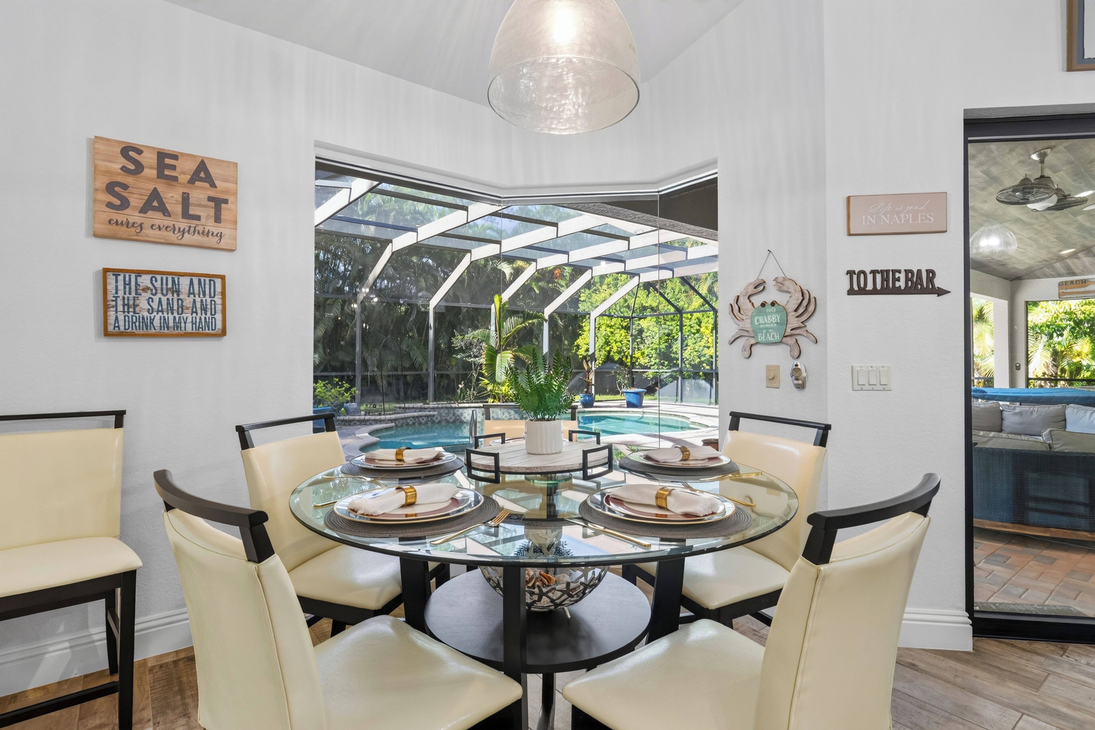 A dining area with a glass table surrounded by chairs, a view of a swimming pool, and decorative wall art.