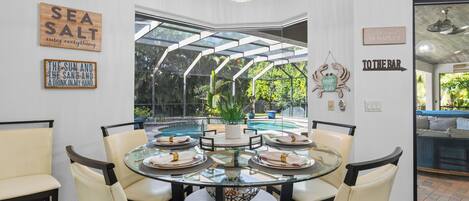 A dining area with a glass table surrounded by chairs, a view of a swimming pool, and decorative wall art.