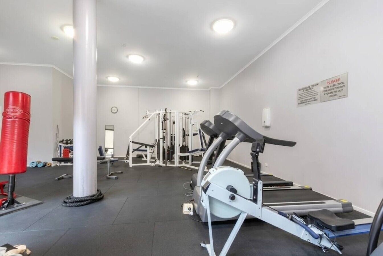 Academia com equipamentos de cardio, máquinas de musculação e um saco de pancadas vermelho.