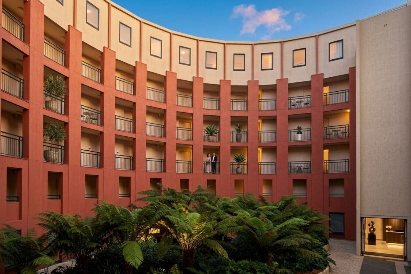A multi-story building with balconies, some with plants, and a clear sky.