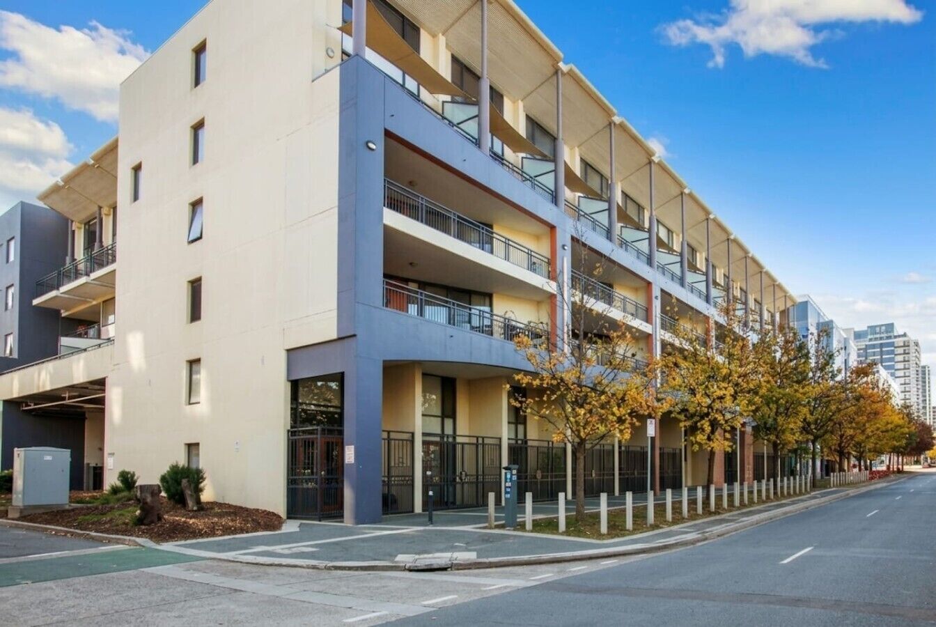 Un edificio residencial de varios pisos con balcones, un acceso con portón y una zona de estacionamiento.