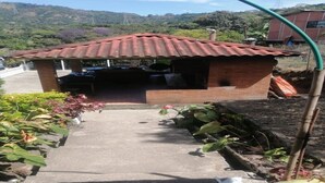 Una pequeña construcción de ladrillo con techo de metal corrugado, posiblemente una cocina o espacio de almacenamiento, con un sendero de hormigón que la conduce.