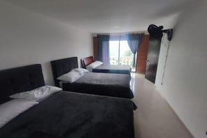 Een hotelkamer met twee bedden, een groot raam met gordijnen en uitzicht op buiten.