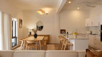 A modern kitchen with white cabinets, a dining area with wooden furniture, and a ceiling fan.