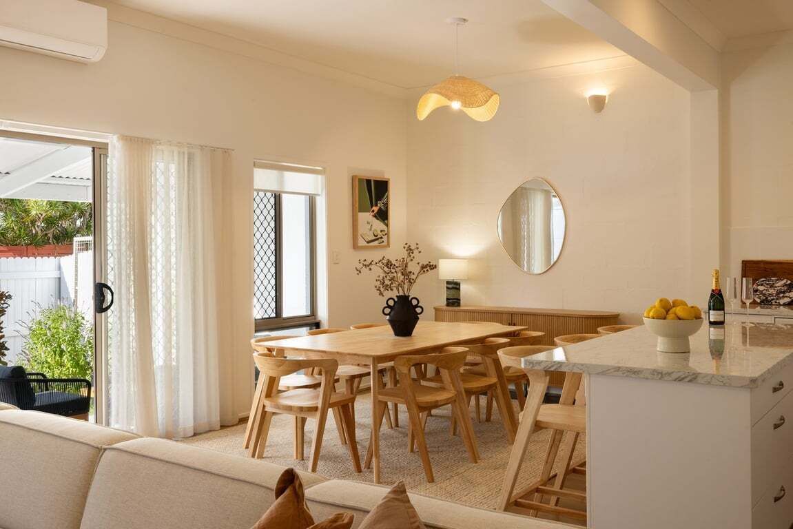 A modern kitchen with a dining area, featuring a wooden table and chairs, a built-in island with a sink, and a large mirror above the island.
