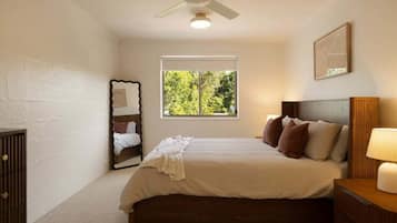 A bedroom with a bed, a window, a ceiling fan, a bedside table, and a dresser.