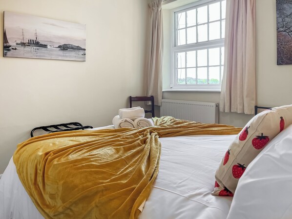 A hotel room with a bed, a window with curtains, a radiator, and a painting on the wall.