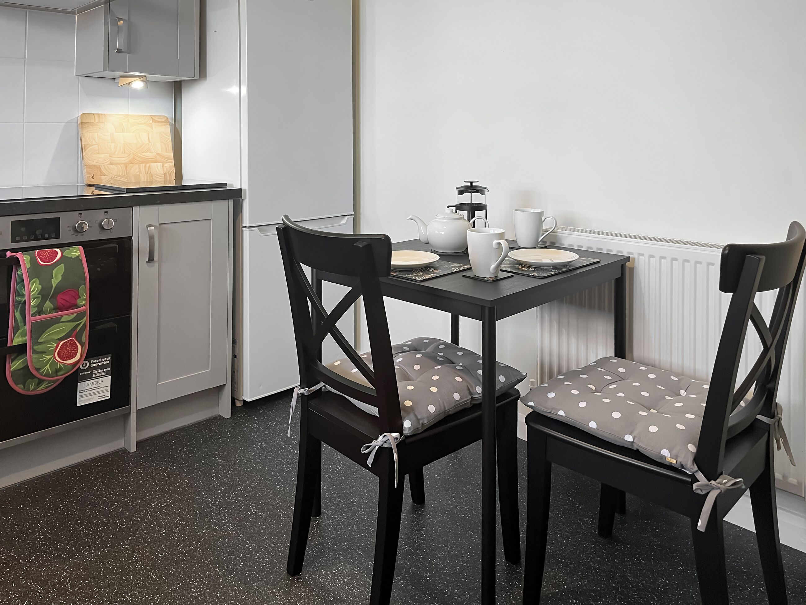 Eine kompakte Küche mit Essbereich, ausgestattet mit einem Kühlschrank, Backofen und einem Tisch, gedeckt mit Tellern und einem Teekännchen.