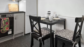 Eine kompakte Küche mit Essbereich, ausgestattet mit einem Kühlschrank, Backofen und einem Tisch, gedeckt mit Tellern und einem Teekännchen.
