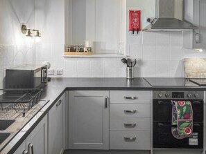 A modern kitchen with a dishwasher, oven, and a microwave. There is a fire blanket on the wall and a knife block on the countertop.