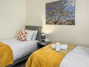 Une chambre d’hôtel avec deux lits, une table de chevet, une lampe et un tableau représentant un arbre.