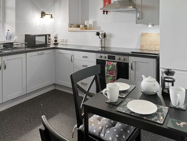 Une cuisine moderne avec des meubles blancs, un plan de travail noir et un coin repas avec une table dressée pour deux personnes.