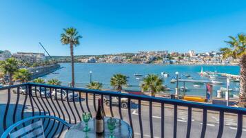 Un balcone con tavolo, sedie e una bottiglia di vino, con vista su una marina piena di barche e una cittadina costiera.