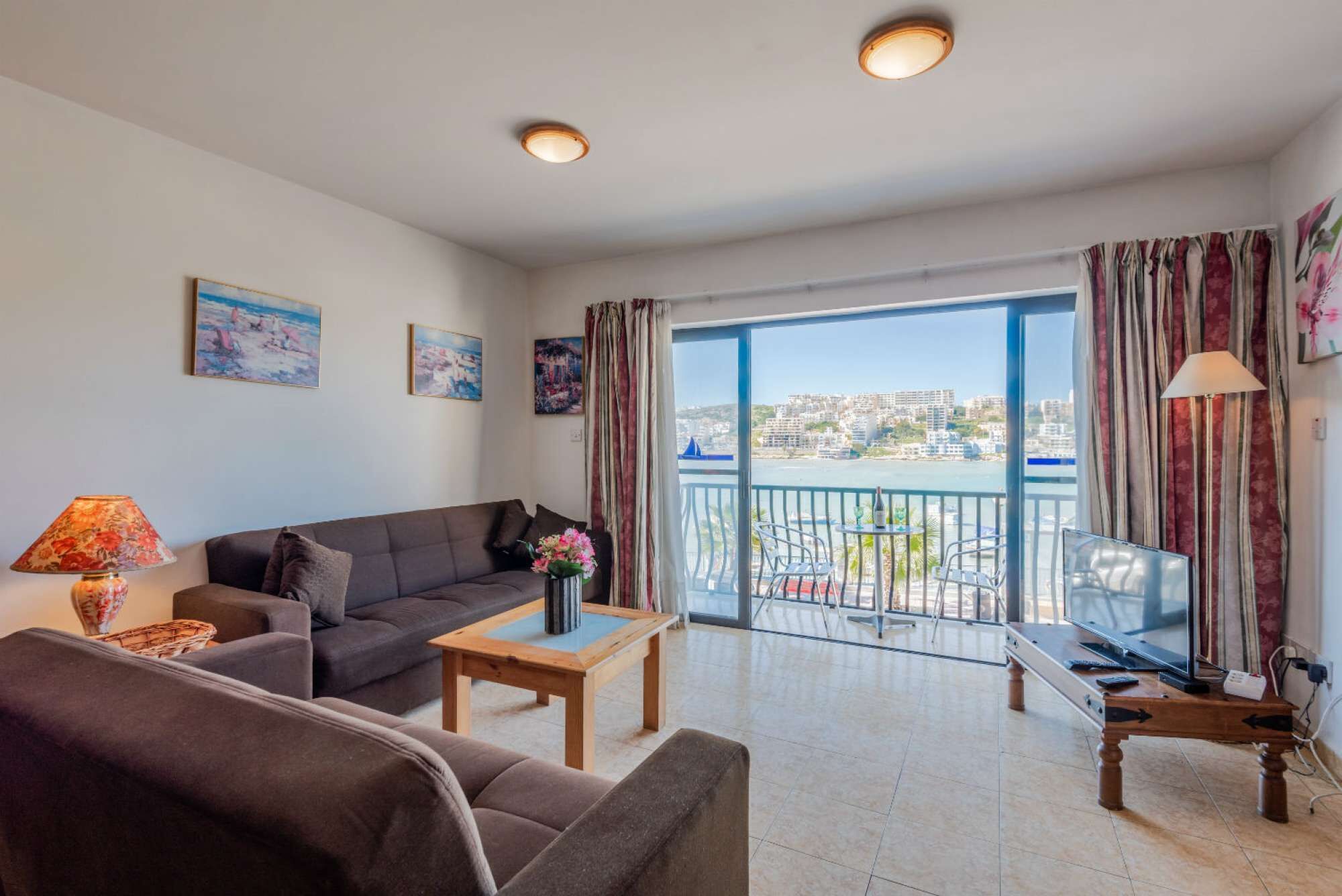 Ein Wohnzimmer mit Sofa, Couchtisch, Fernseher und einem Balkon mit Blick auf die Stadt.