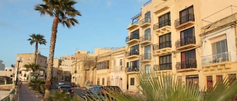 Una calle bordeada de edificios de varios pisos, algunos con balcones, y palmeras.