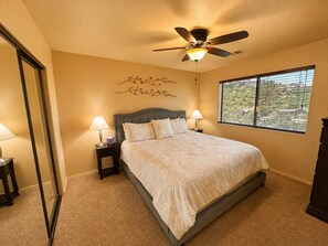 A bedroom with a bed, two bedside lamps, a ceiling fan, a window with blinds, and a decorative wall piece. - The Prescott Social + Near Whiskey Row + Views (Prescott)