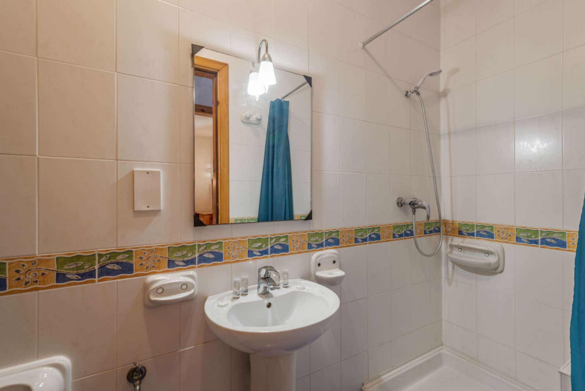 Une salle de bain avec un lavabo blanc, un miroir, une douche et des toilettes.