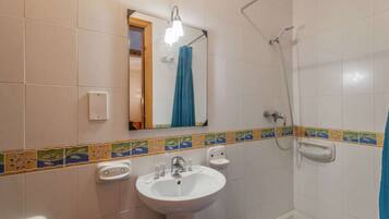Une salle de bain avec un lavabo blanc, un miroir, une douche et des toilettes.