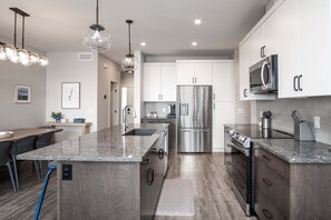 A modern kitchen with a central island, stainless steel appliances, and pendant lighting. - 3BR Kelowna townhome with lakeview, mountain views, deck, BBQ, Wi-Fi, and parking. (Kelowna)