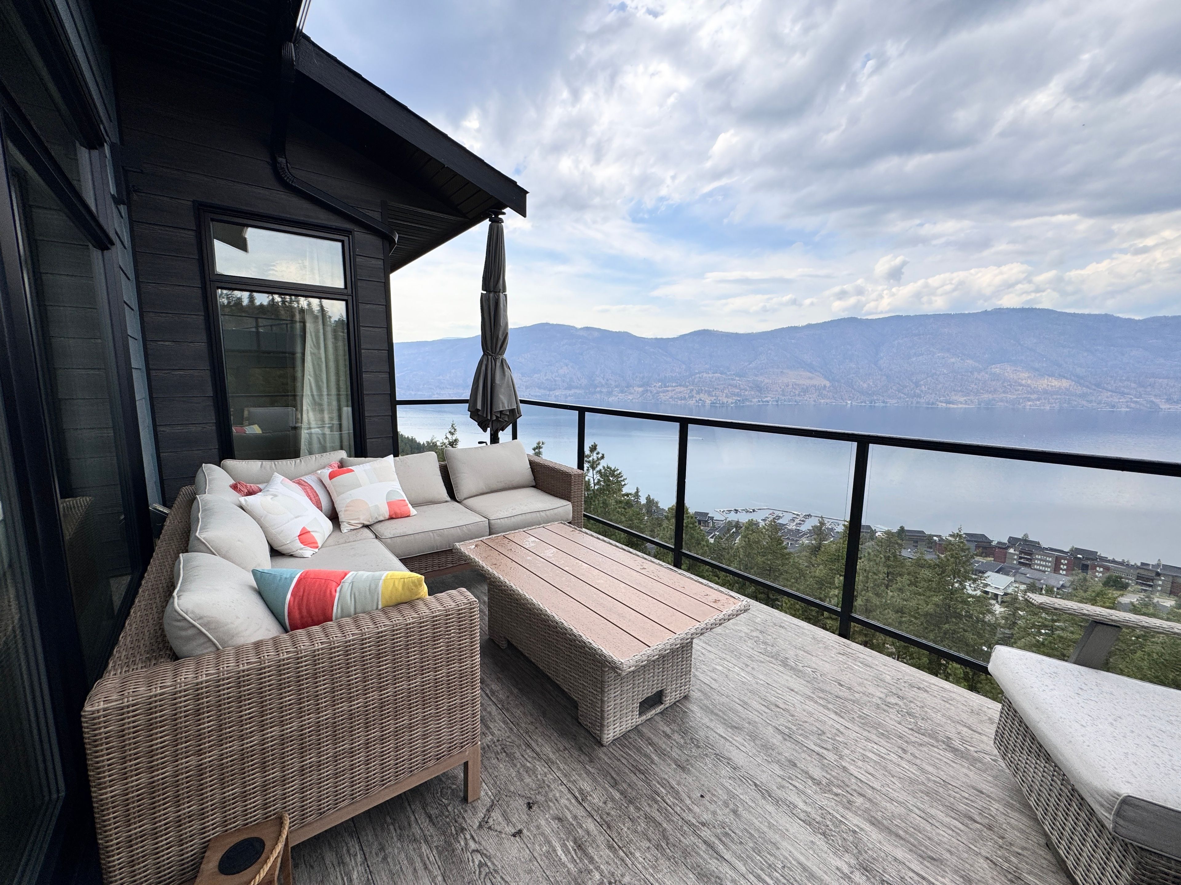 A balcony with wicker furniture, a view of a lake, and mountains in the distance.