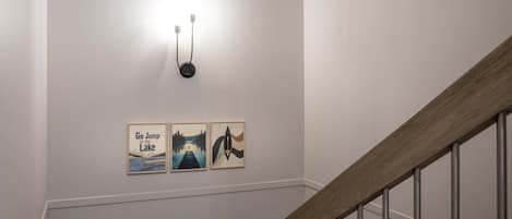 A staircase with a wooden handrail and metal balusters, leading to a landing with a wall-mounted light fixture and three framed artworks.