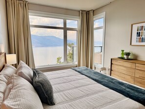 A bedroom with a bed, a dresser, a window with a view of a lake and mountains, and a lamp. - 3BR Kelowna townhome with lakeview, mountain views, deck, BBQ, Wi-Fi, and parking. (Kelowna)