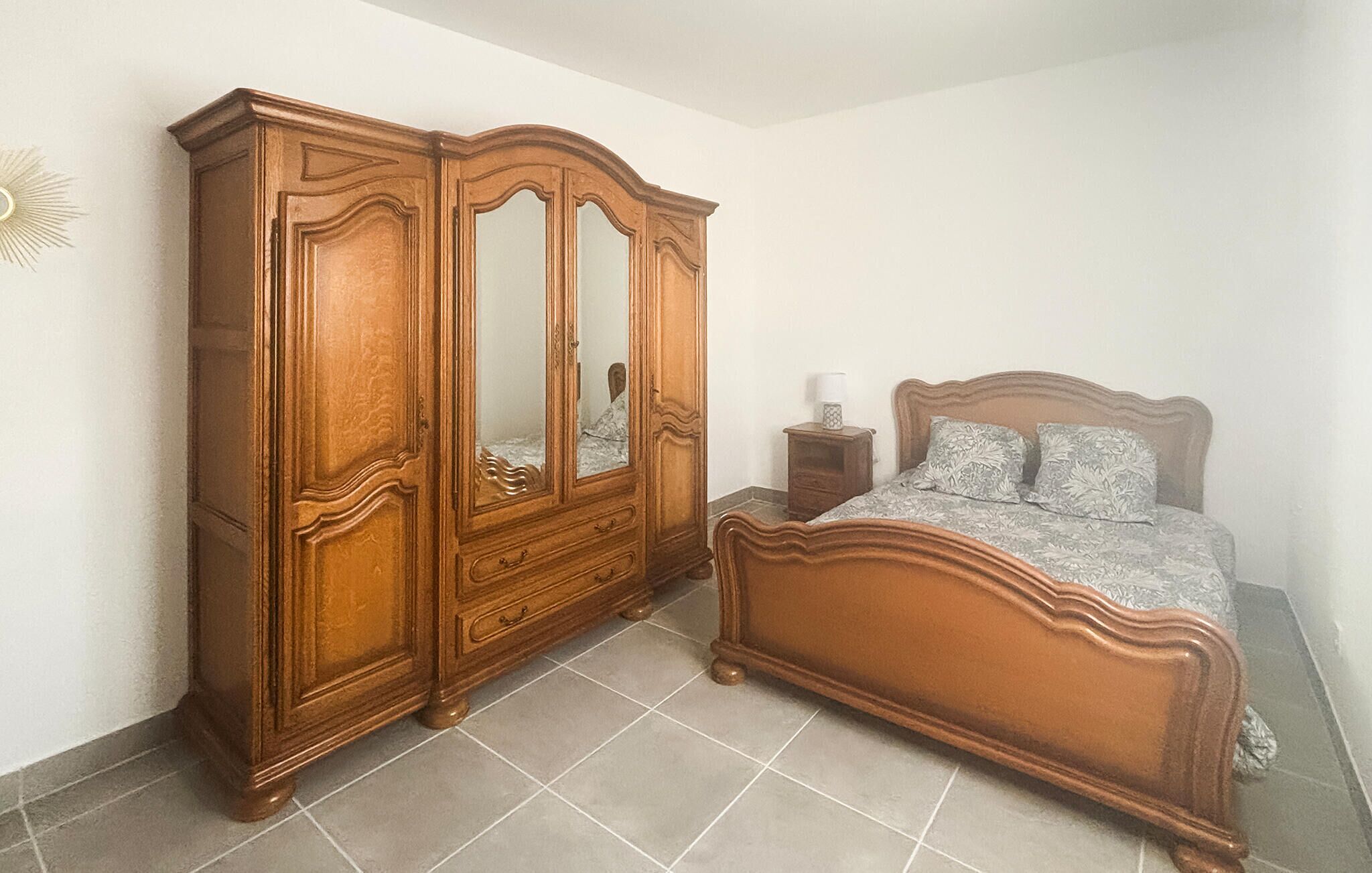 A bedroom with a wooden wardrobe, a bed with a headboard, and a nightstand with a lamp.