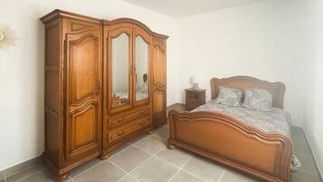A bedroom with a wooden wardrobe, a bed with a headboard, and a nightstand with a lamp.