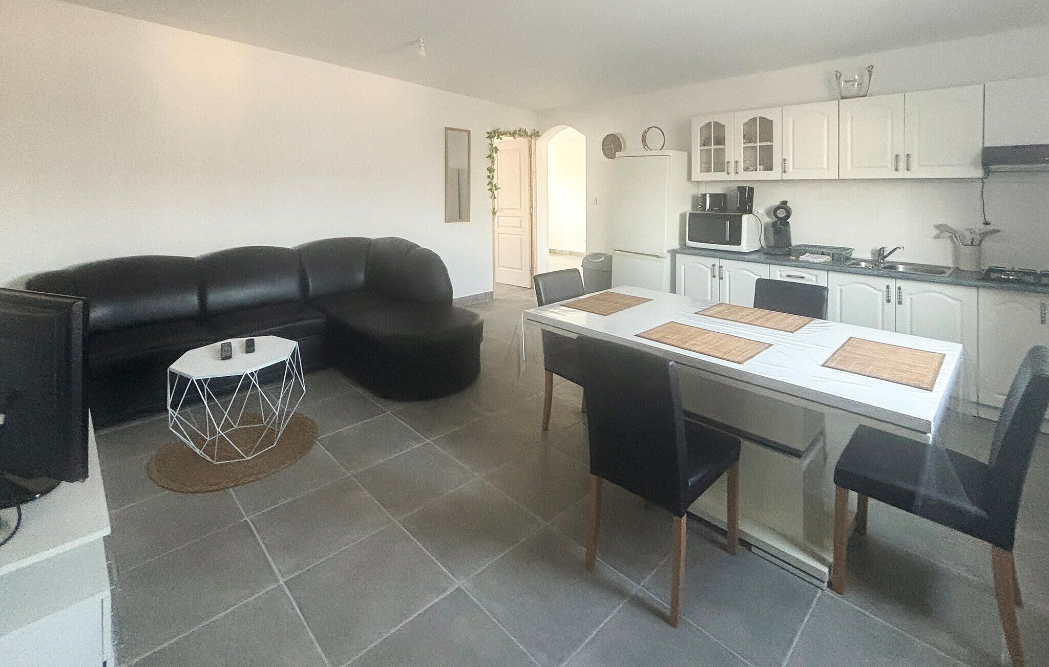 A compact living space with a sofa, dining table, chairs, and a kitchen area.