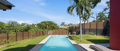 A rectangular swimming pool with a wooden fence and palm trees in the background.