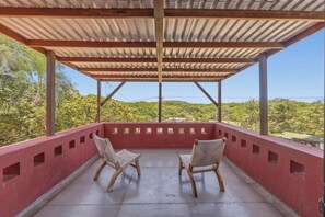 A covered outdoor seating area with two wooden chairs and a view of a green landscape. - 3 bdm*3.5 bath*short walk to the beach*pool*quiet (Tamarindo)