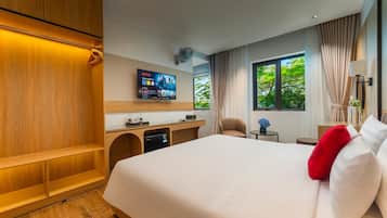A hotel room with a large bed, a desk with a flat-screen TV, a seating area, and a window with a view of trees.