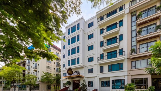 Um hotel com vários andares, uma entrada destacada, uma escadaria que leva à entrada principal e uma área de estacionamento em frente.
