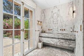 A bathroom with a marble sink, a shower, and a view of a garden through a glass door. - Villa Shaily  300m Pampelonne Beach and Club 55 (Ramatuelle)