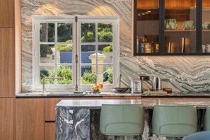 A kitchen with a marble backsplash, a window with a view of greenery, and a bar area with bottles and glasses. - Villa Shaily  300m Pampelonne Beach and Club 55 (Ramatuelle)