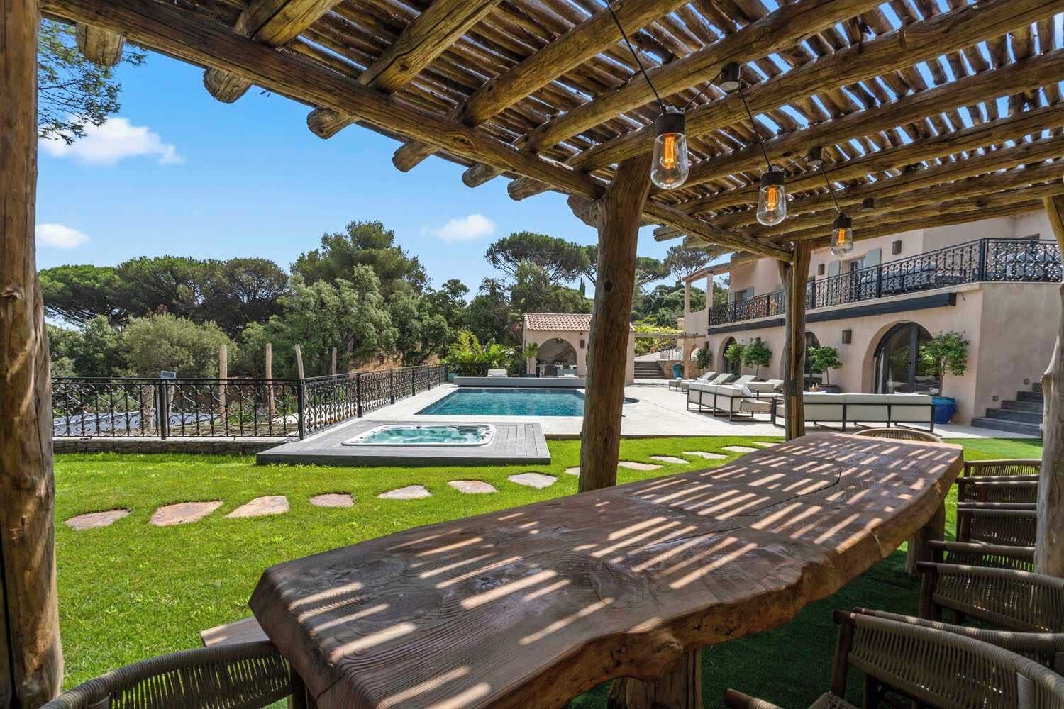 Eine Holz-Pergola mit hängenden Lichtern, einem Pool und Sitzgelegenheiten im Freien.