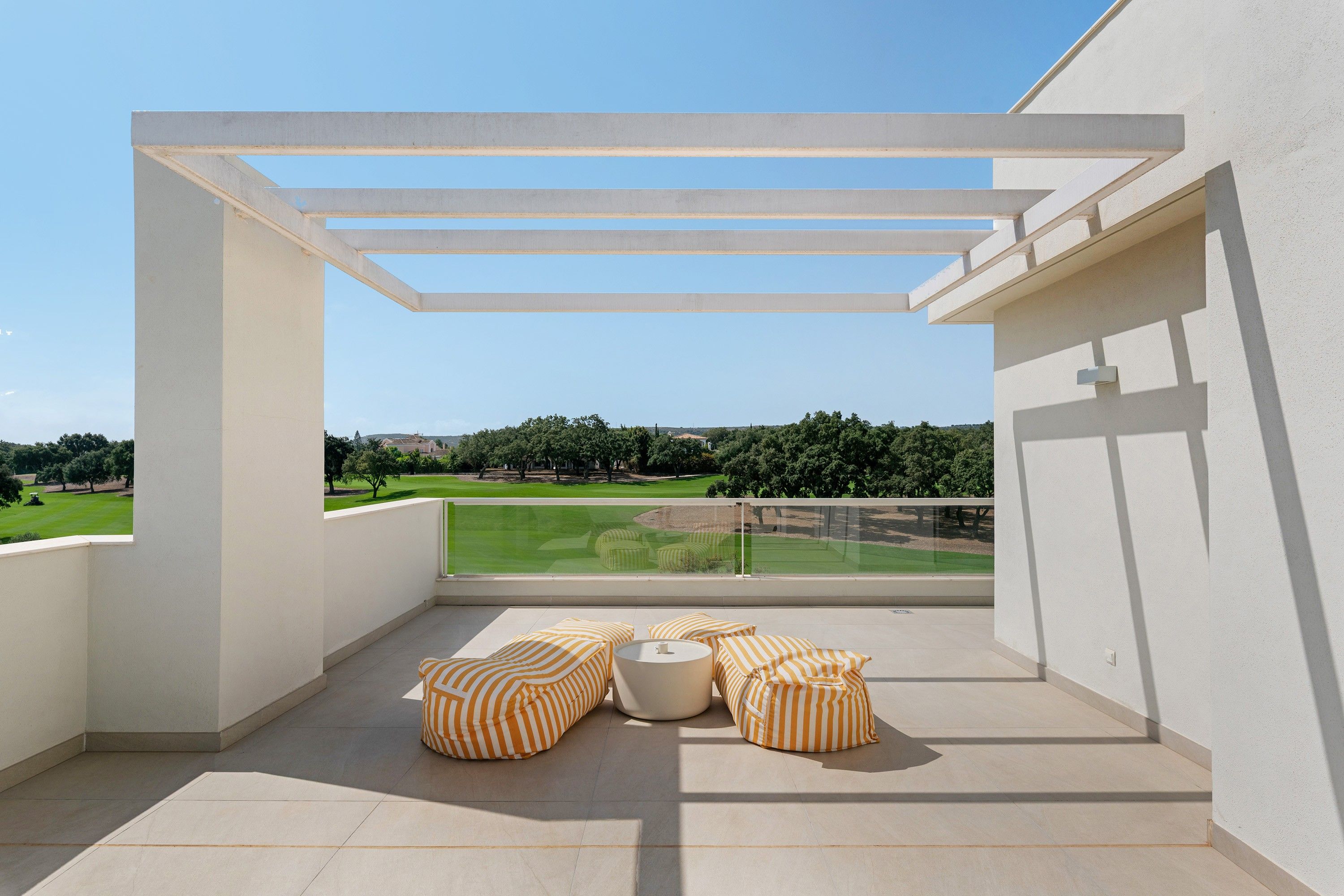 Un balcón con vistas a un paisaje verde, que incluye una pérgola blanca y cojines a rayas.