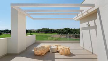 Un balcón con vistas a un paisaje verde, que incluye una pérgola blanca y cojines a rayas.