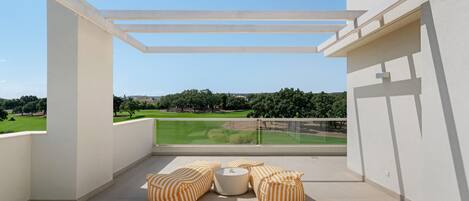 Un balcón con vistas a un paisaje verde, que incluye una pérgola blanca y cojines a rayas.