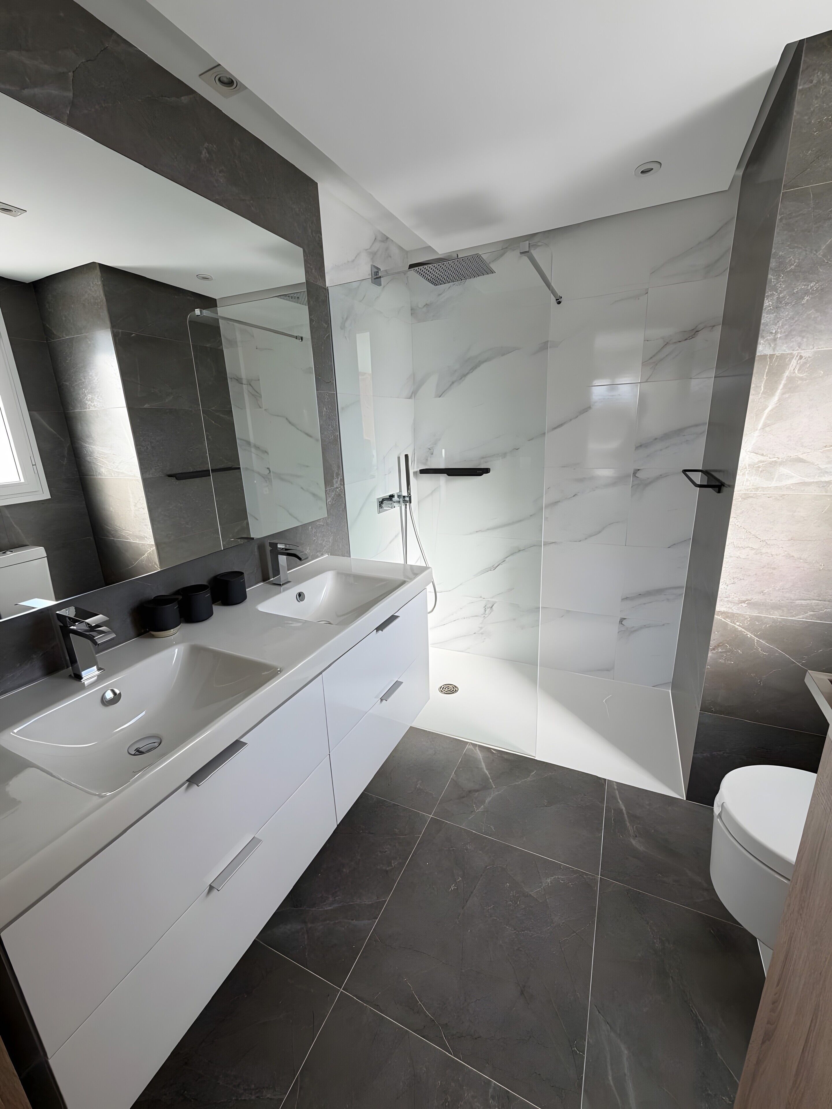 Un baño moderno con tocador doble, ducha con cerramiento de vidrio y un inodoro.