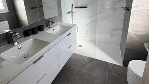 A modern bathroom with a double sink vanity, a glass-enclosed shower, and a toilet. - Holiday Home 'Beautiful House in Emerald Green' with Sea View, Wi-Fi and Air Conditioning (San Roque)
