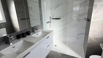 Un baño moderno con tocador doble, ducha con cerramiento de vidrio y un inodoro.