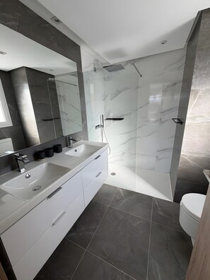 Un baño moderno con tocador doble, ducha con cerramiento de vidrio y un inodoro.