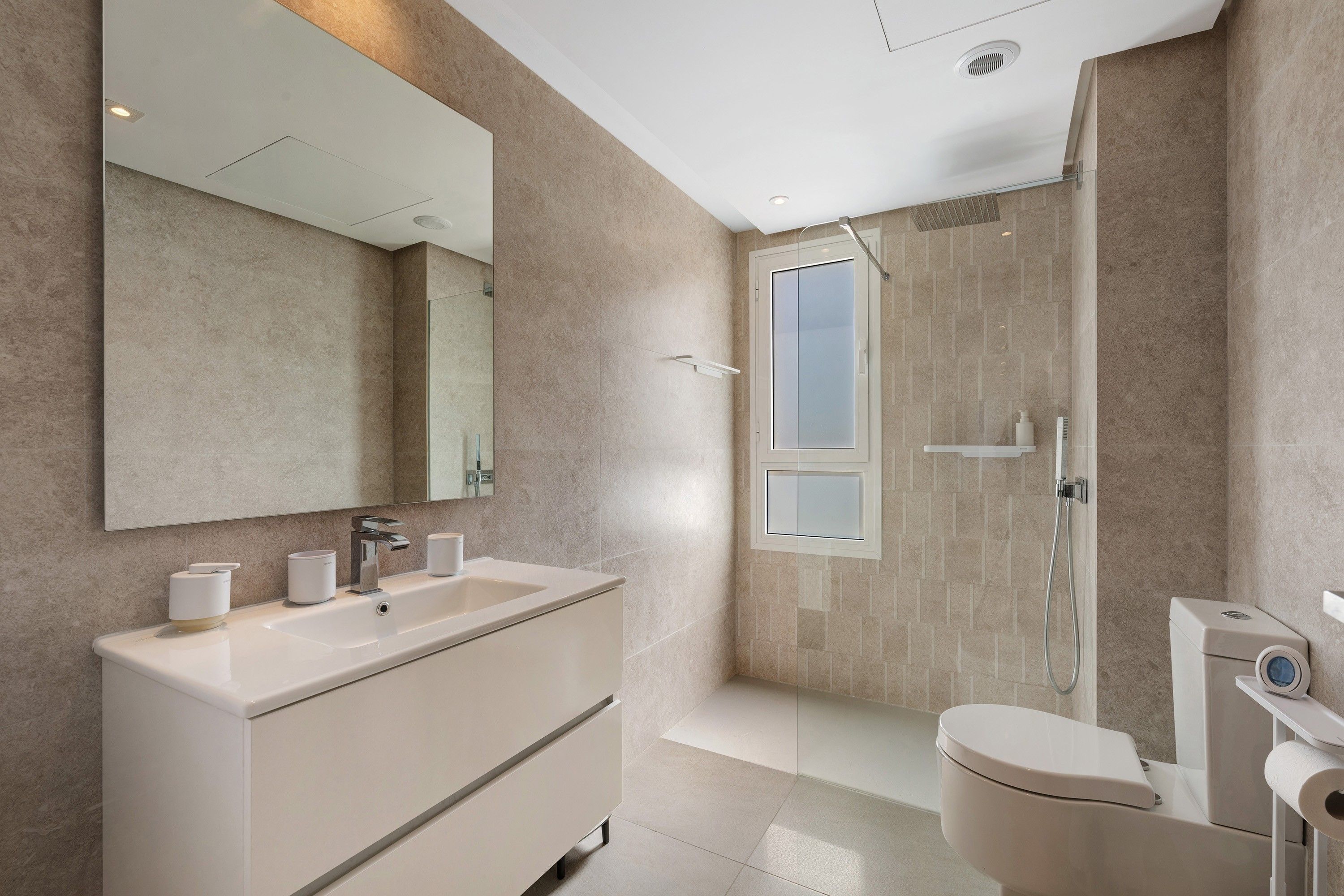 Un baño moderno con un espejo grande, un lavamanos, un inodoro y una zona de ducha.