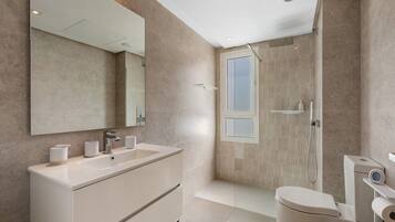 Un baño moderno con un espejo grande, un lavamanos, un inodoro y una zona de ducha.