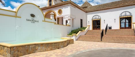 Un edificio con una fuente de piedra, una escalera y un letrero que dice 'The San Roque Club'.